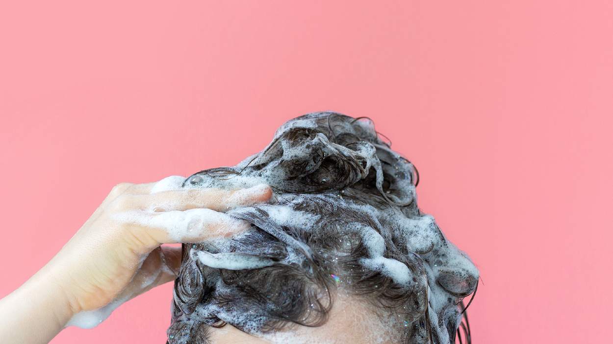 Mujer lavándose el cabello con fondo de color rosa