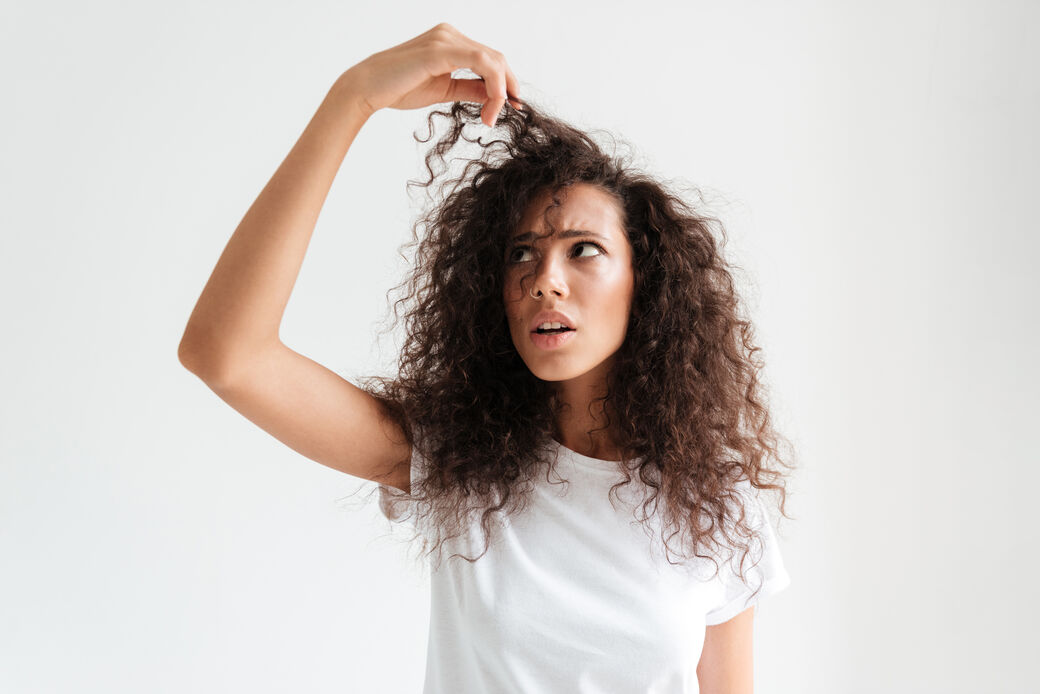 Retrato de una joven confundida que se examina el pelo mientras está de pie aislada sobre fondo blanco