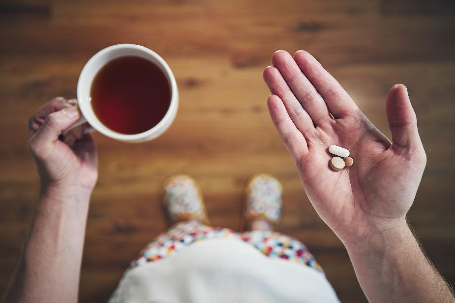 Hombre con fármacos en la mano y una taza de té