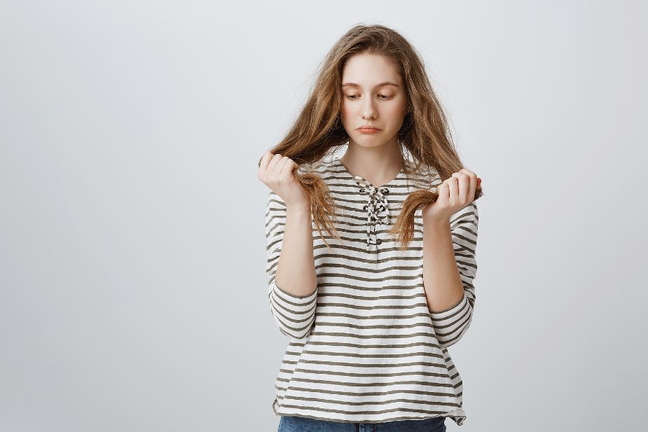 Mujer con problemas en el cabello mirándose el pelo y sujetándolo con las dos manos