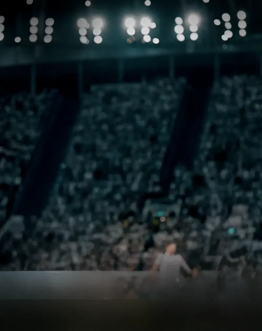Vista borrosa de un estadio de fútbol lleno por la noche, con potentes reflectores y gradas abarrotadas